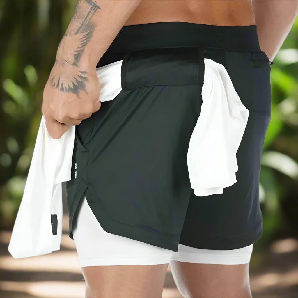 Man wearing black 2-in-1 gym shorts with a white towel tucked into the waistband.