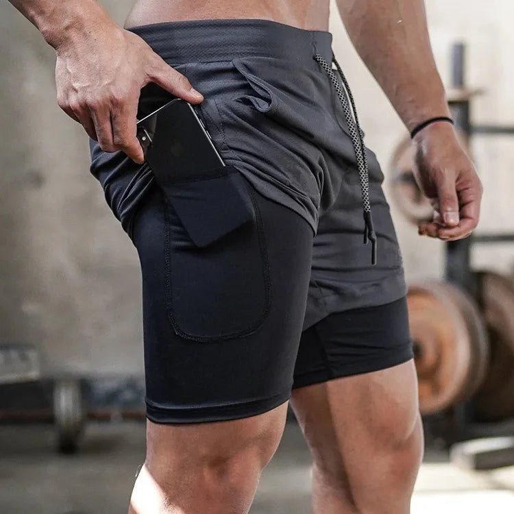 Man wearing black 2-in-1 gym shorts, placing a phone in the side pocket of the black inner compression layer