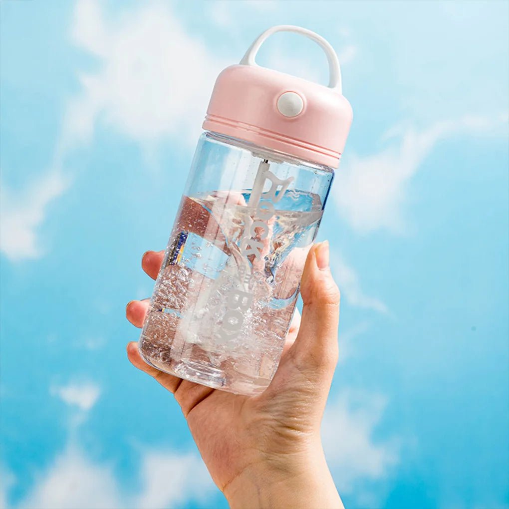 Hand holding a clear electric shake bottle with a pink lid, blending water against a blue sky background.