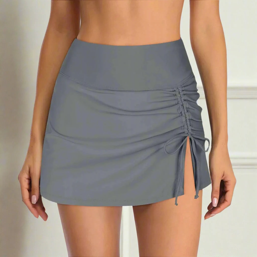 Light gray swim skirt with ruched side detailing and adjustable drawstring, offering a stylish and customizable fit for beach and poolside activities.