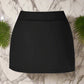 Black high-waisted swim skirt with a smooth, elegant design, set against a marble backdrop with green fern accents, ideal for stylish beachwear.