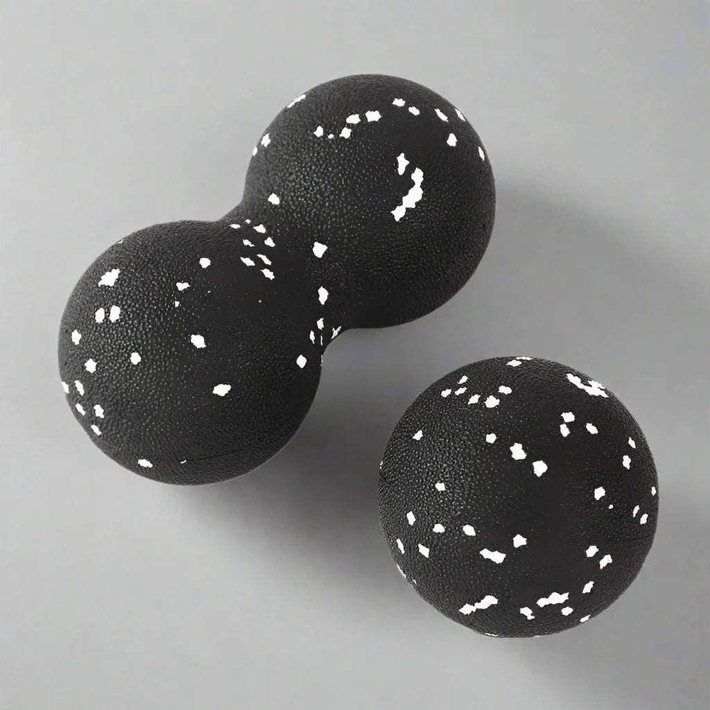 Black double and single massage balls with white speckles, designed for deep tissue massage and muscle relief, placed on a neutral grey background.