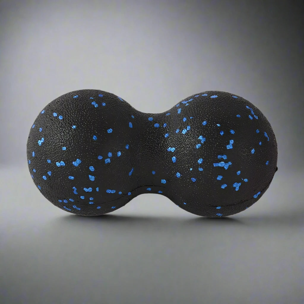 Black double massage ball with blue speckles, used for muscle relaxation and deep tissue therapy, placed on a gradient grey background.