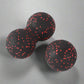 Black double massage ball with red speckles, ideal for deep tissue muscle therapy and relaxation, placed on a neutral background.