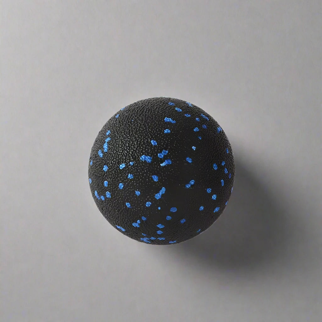 Black massage ball with blue speckles, designed for muscle relief and therapy, placed against a light grey background.