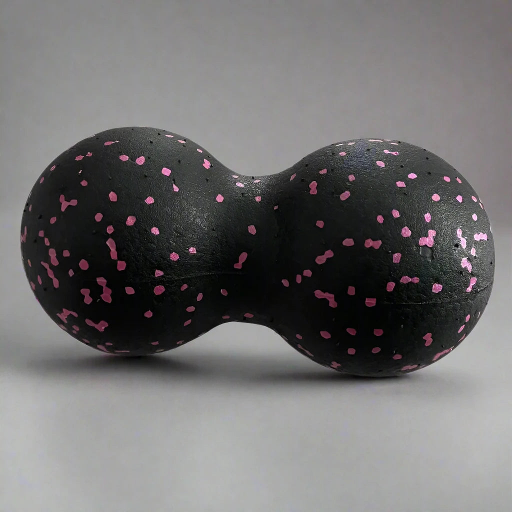 Black double massage ball with pink speckles, designed for muscle relaxation and deep tissue therapy, placed on a light grey background.