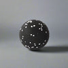 Black massage ball with white speckles, designed for muscle relief and massage therapy, placed against a plain grey background.