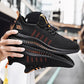 A close-up shot of a pair of black lightweight running shoes with orange accents and a textured sole, being held by a person in an urban setting. The sneakers feature a breathable mesh upper and a modern, streamlined design.