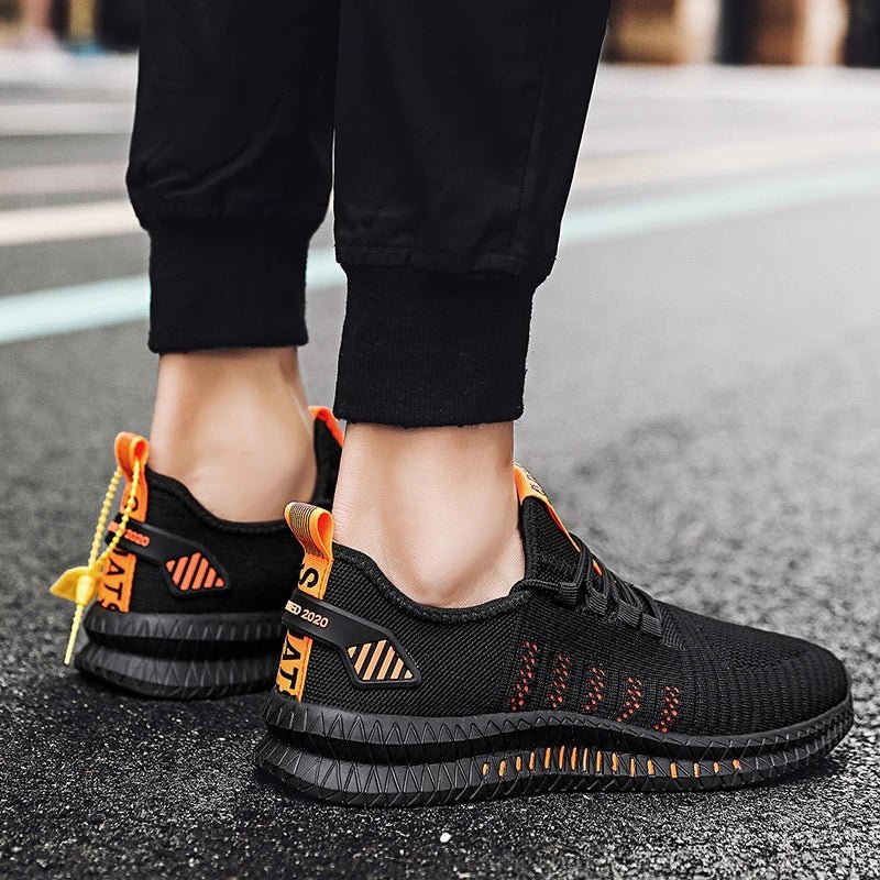 Back view of a person wearing black and orange lightweight men's running shoes, featuring a breathable mesh upper and durable, slip-resistant sole, while standing on a wet street pavement.