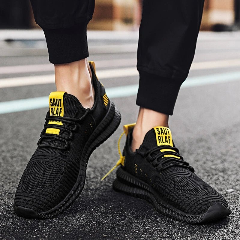 Person wearing black and yellow lightweight men's running shoes with breathable mesh design, slip-resistant sole, and flexible laces, walking on a street pavement.