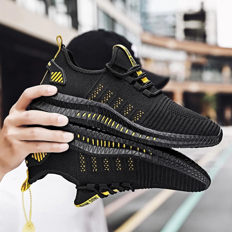 A pair of black lightweight running sneakers with yellow accents and a textured sole design, held in hand, ideal for male athletes looking for breathable, comfortable footwear.